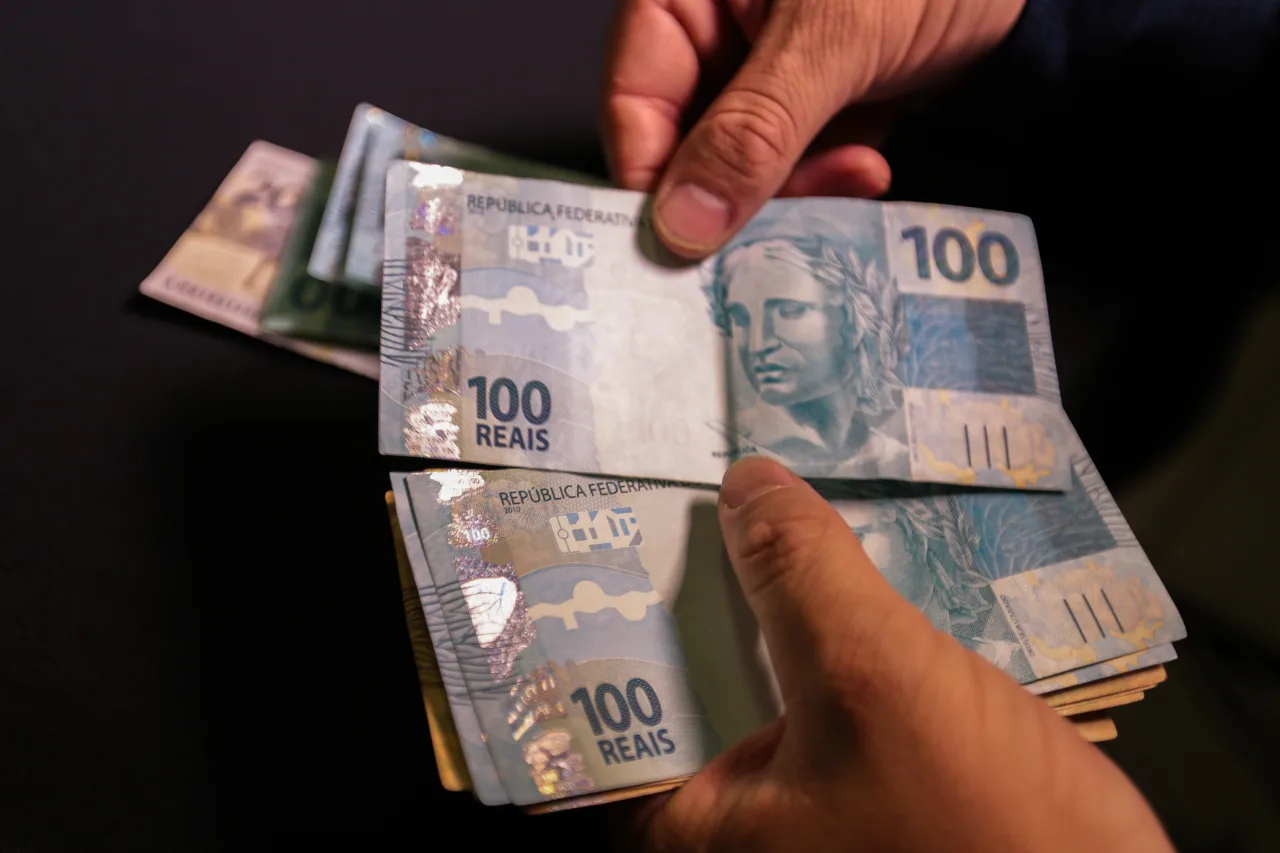 Notas de cem reais empilhadas sobre uma mesa.