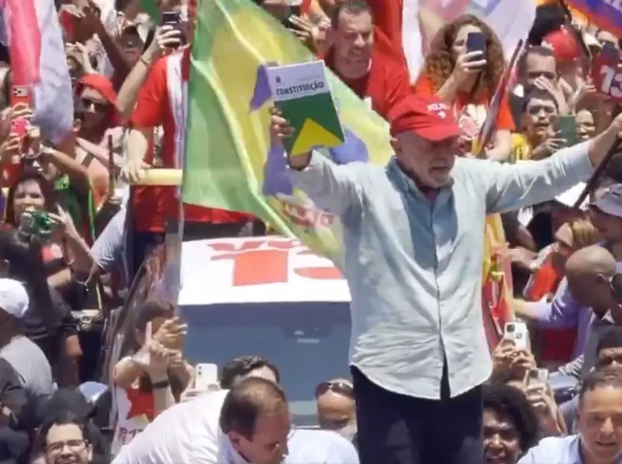 Luiz Inácio Lula da Silva segurando a Constituição Federal e uma bandeira do Brasil no Rio de Janeiro.
