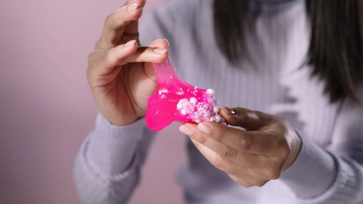 Criança manuseando massa de slime colorida em ambiente doméstico.